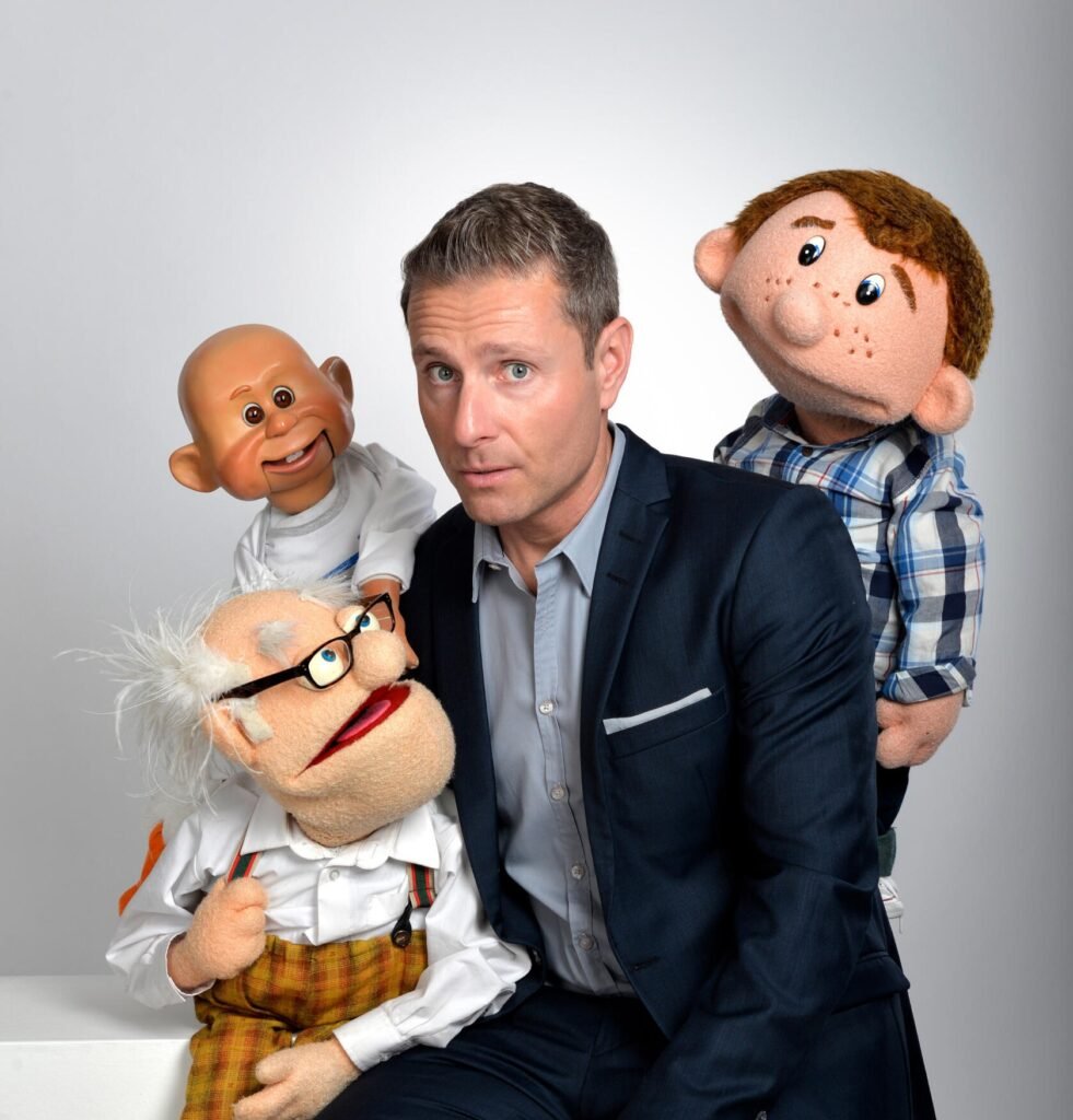 A man sits on a plinth surrounded by three puppets.