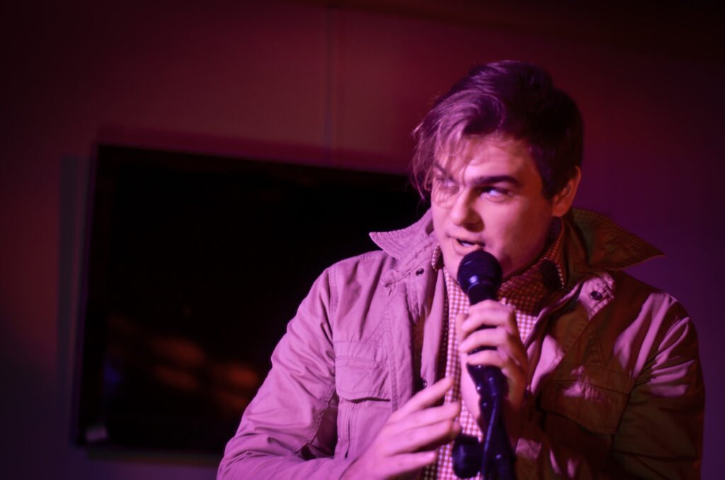 man on a microphone telling a joke under a purple light wash